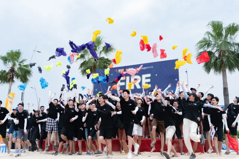 BSS team members on a beach tossing colorful items into the air in front of a FIRE banner and palm trees