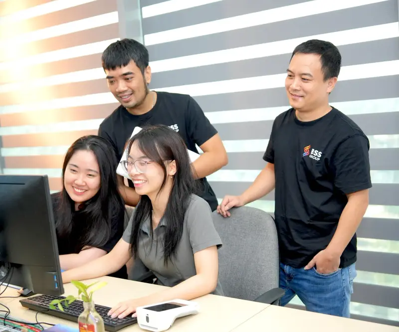 Four BSS colleagues in BSS T-shirts talking around a desk in the office